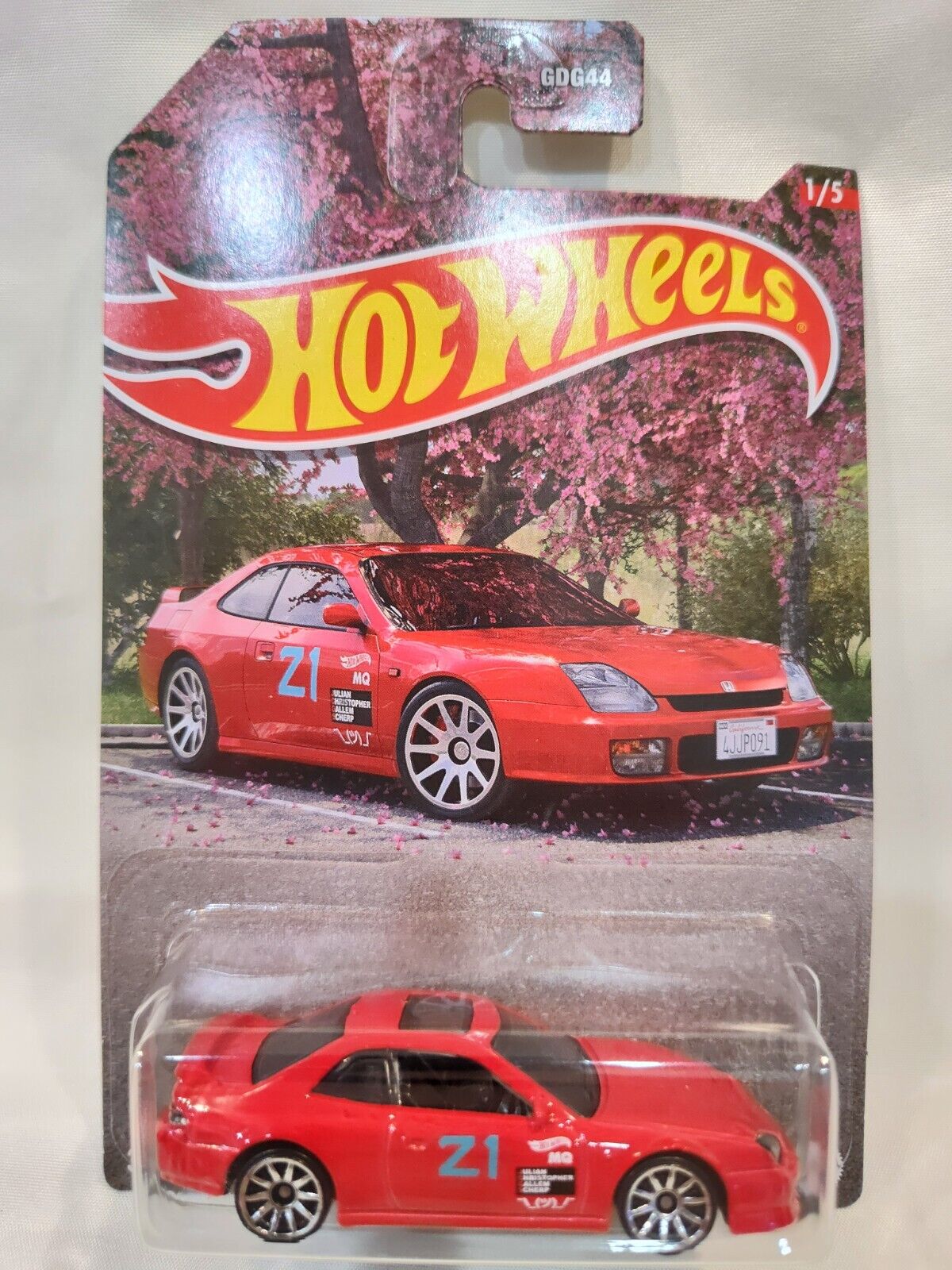 The Hot Wheels 1:64 Walmart Exclusive Theme JDM features a red sports car with “21” and racing decals, packaged with pink blossoming trees in the background and the Hot Wheels logo at the top.